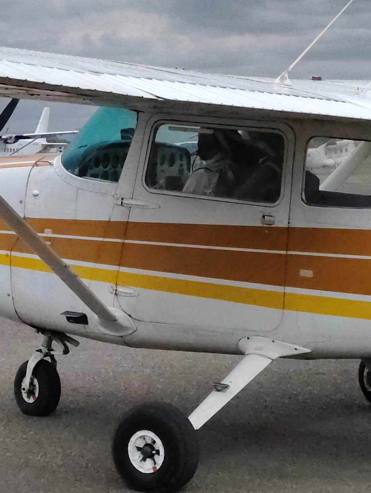 A white Cessna with orange and yellow stripes taxiing on the apron