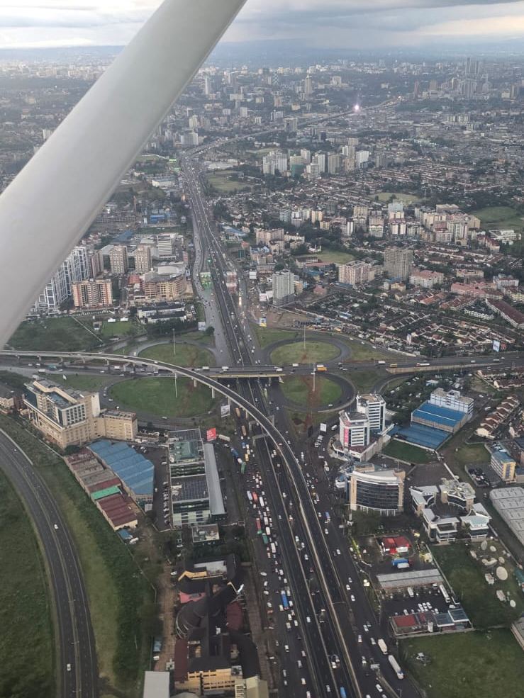 Aerial view of a Nairobi highway interchange and the city skyline beneath an aircraft wing strut
